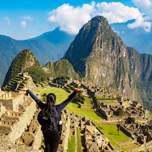A happy woman with raised arms enjoying the view of Machu Picchu Citadel in Peru